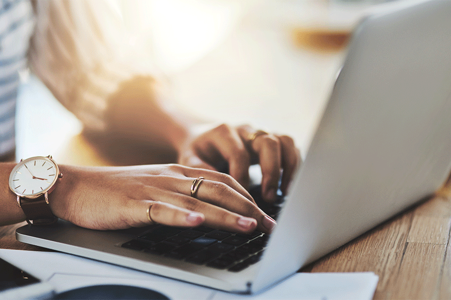 Detailed image of the hands of a Black female typing on a laptop computer. 